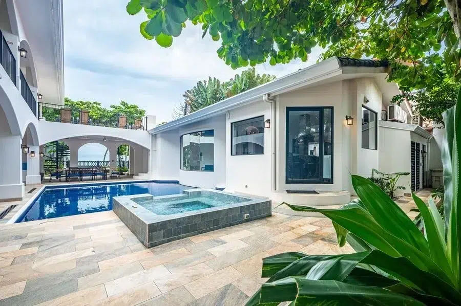fotografia-para-propiedades-espacios-31 | Pacific Photography Casa blanca moderna con piscina rectangular y spa elevado, rodeada por un patio de baldosas de piedra y exuberante vegetación.