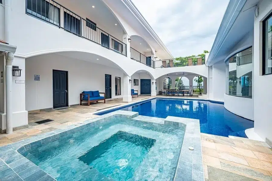 fotografia-para-propiedades-espacios-32 | Pacific Photography Patio de hotel con una piscina rectangular azul, spa/jacuzzi en primer plano y pasarelas arqueadas blancas arriba.