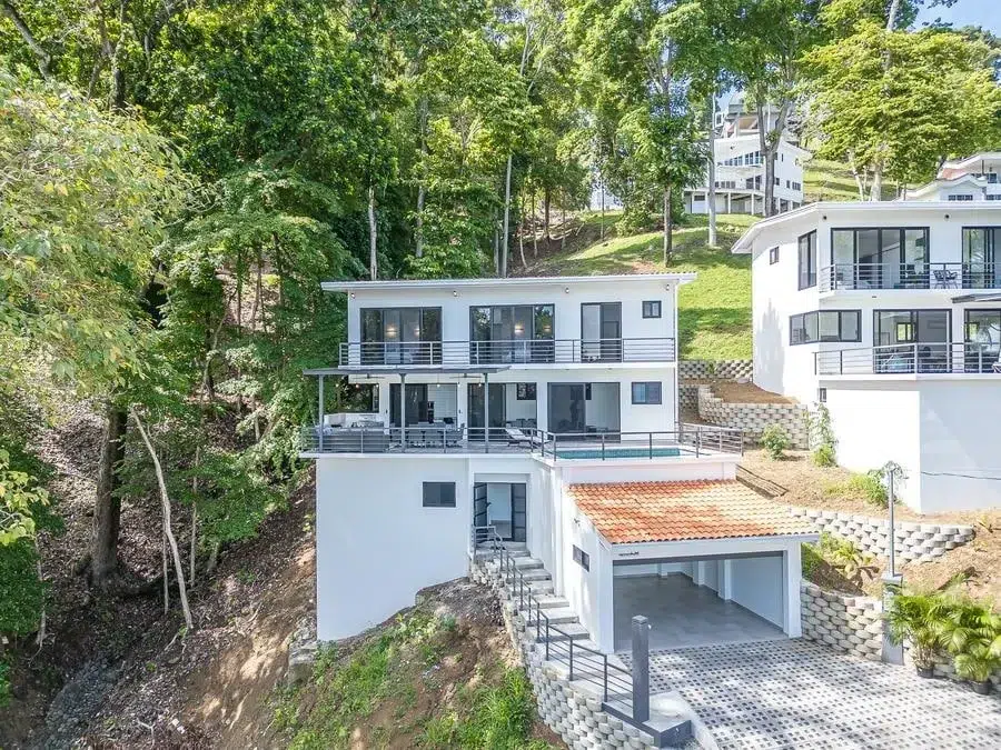 fotografia-para-propiedades-espacios-33 | Pacific Photography Villa moderna blanca en la ladera con múltiples balcones y terrazas con frente de vidrio en medio de árboles y otras casas blancas en una pendiente.