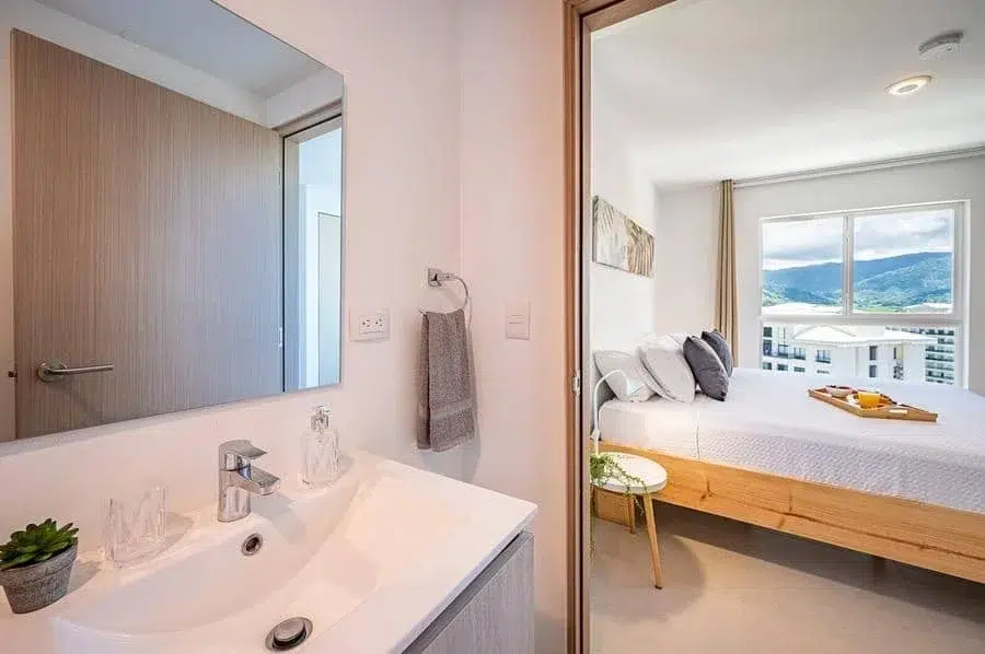 fotografia-para-propiedades-espacios-40 | Pacific Photography Área de lavabo de baño con espejo y toallero que se abre a un dormitorio luminoso con vista a la montaña fuera de la ventana.