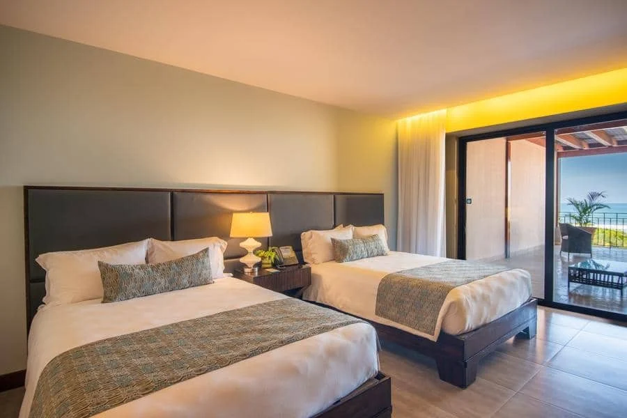 fotografia-para-propiedades-espacios-6 | Pacific Photography Habitación de hotel con dos camas individuales, una mesita de noche compartida y un balcón con vista al mar más allá de las puertas corredizas.