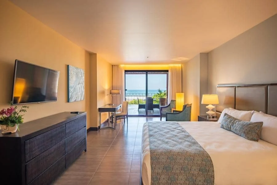 fotografia-para-propiedades-espacios-8 | Pacific Photography Cama king-size en una moderna habitación de hotel, con una cómoda, TV y un balcón con vista al océano.