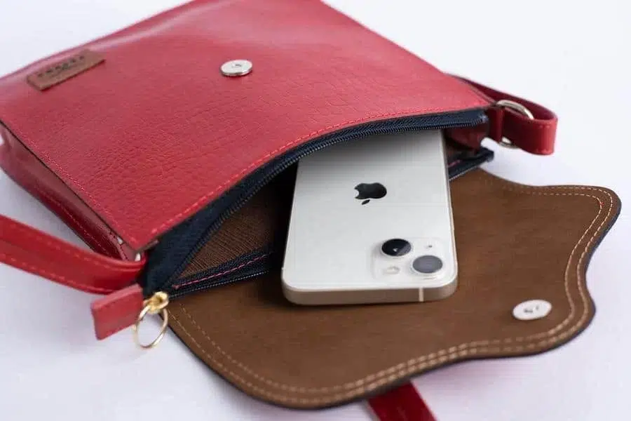 product photography costa rica -1 | Pacific Photography Red leather purse with brown flap open, showing a silver iPhone partially inside the bag's main compartment.
