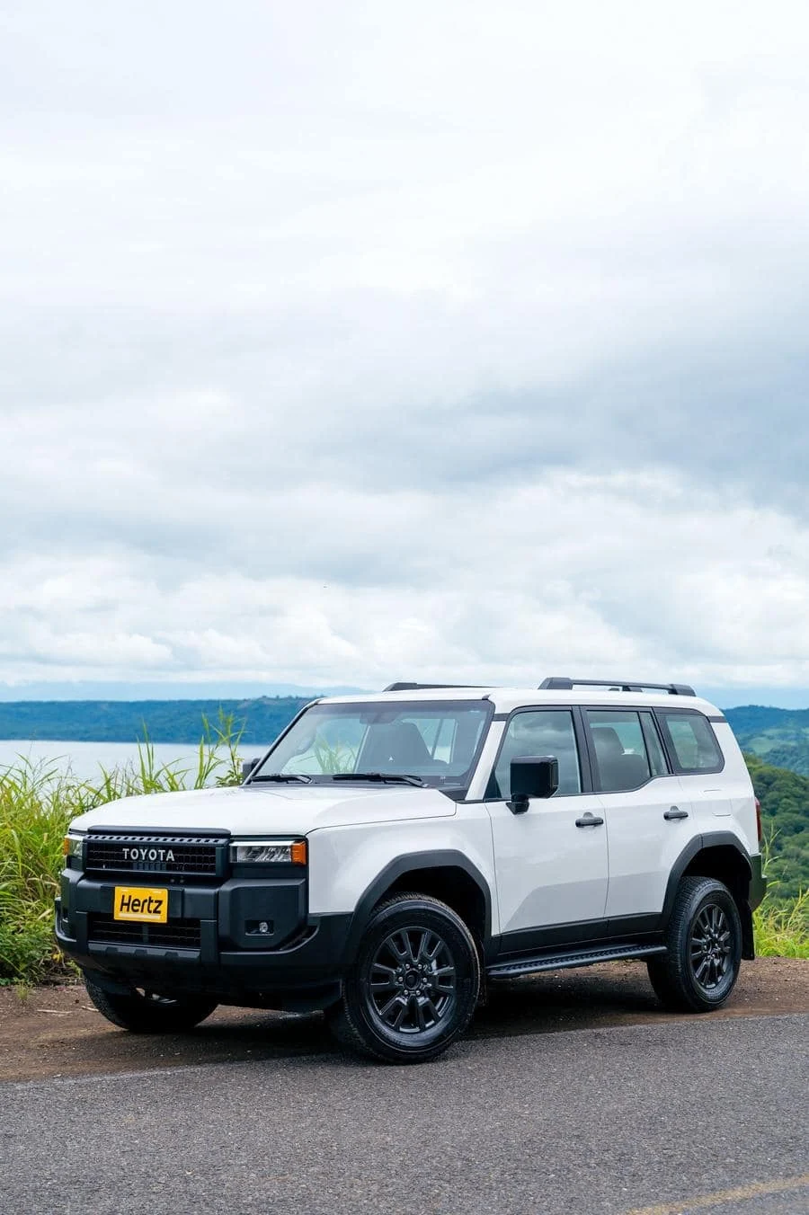 product photography costa rica -11 | Pacific Photography White Toyota SUV parked by the roadside against a cloudy sky and distant hills, with a Hertz rental plate visible on the front bumper.