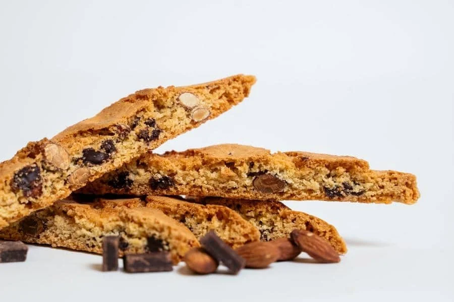 product photography costa rica -16 | Pacific Photography Almond chocolate chip biscotti stacked on a white surface, showing chunky texture and visible almonds and chocolate pieces.