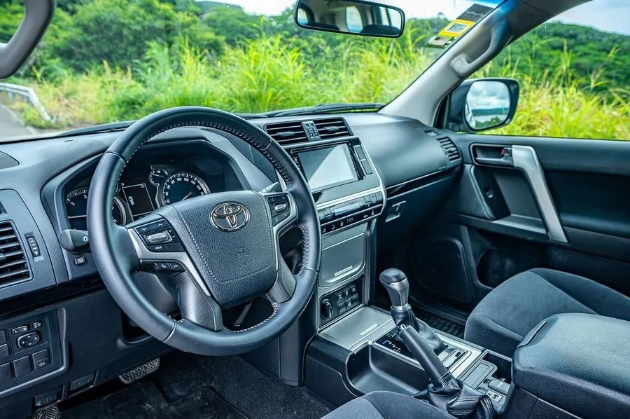 product photography costa rica -5 | Pacific Photography Steering wheel and center console of a Toyota SUV with a touchscreen display and gear shifter, viewed from the driver’s seat with greenery outside the windows.