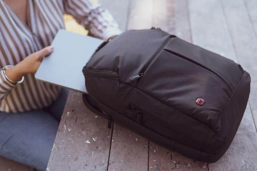 product photography costa rica -9 | Pacific Photography Person places a light blue folder into a black backpack on a wooden bench outdoors.