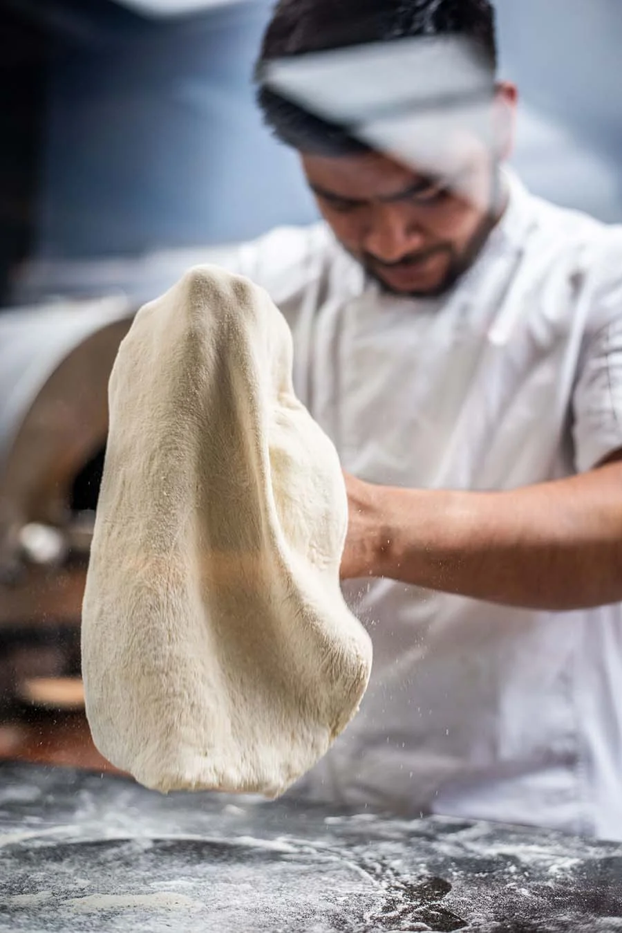 restaurants and hospitality photography costa rica | Pacific Photography Chef tossing dough in a bakery, mid-flip with a flour-dusted countertop nearby.