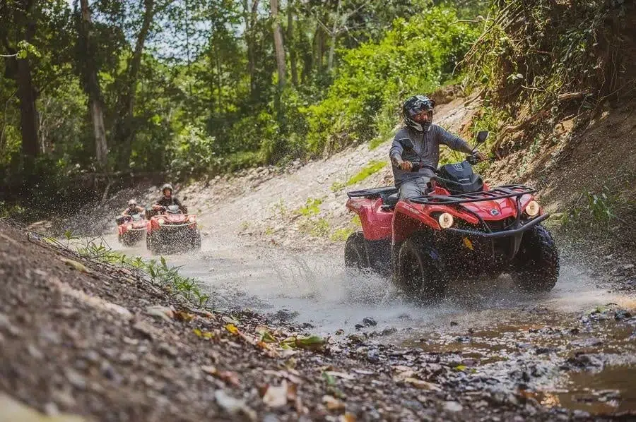 sports and adventure photography costa rica -12 | Pacific Photography Person driving a red ATV through a muddy forest trail with water splashing, followed by other riders