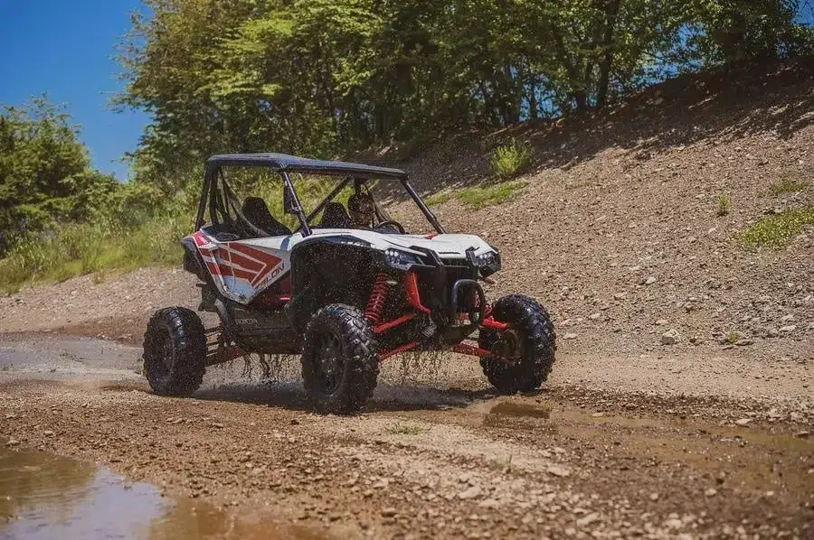 sports and adventure photography costa rica -13 | Pacific Photography Off-road side-by-side buggy kicking up mud on a rocky dirt trail under a sunny blue sky, with trees and a dirt embankment in the background
