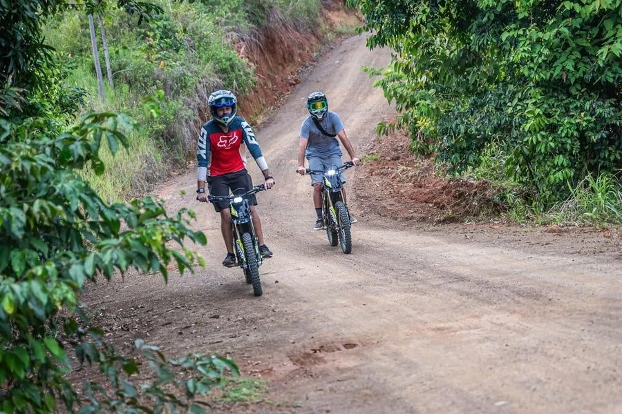 sports and adventure photography costa rica -17 | Pacific Photography Two cyclists wearing helmets ride mountain bikes on a dusty dirt trail through a green forest.