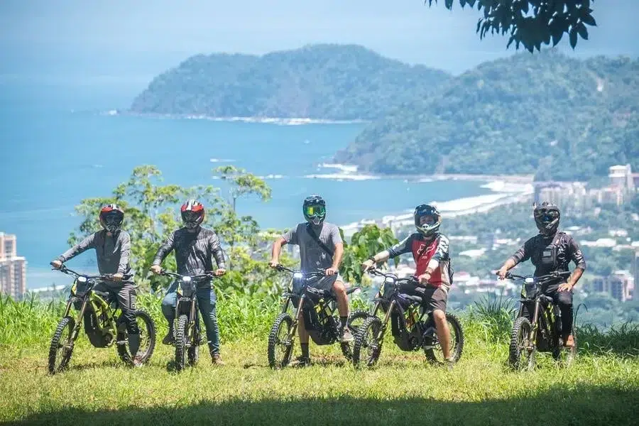 sports and adventure photography costa rica -18 | Pacific Photography Five cyclists wearing helmets sit on mountain bikes on a grassy overlook with a coastal town and blue ocean in the background.