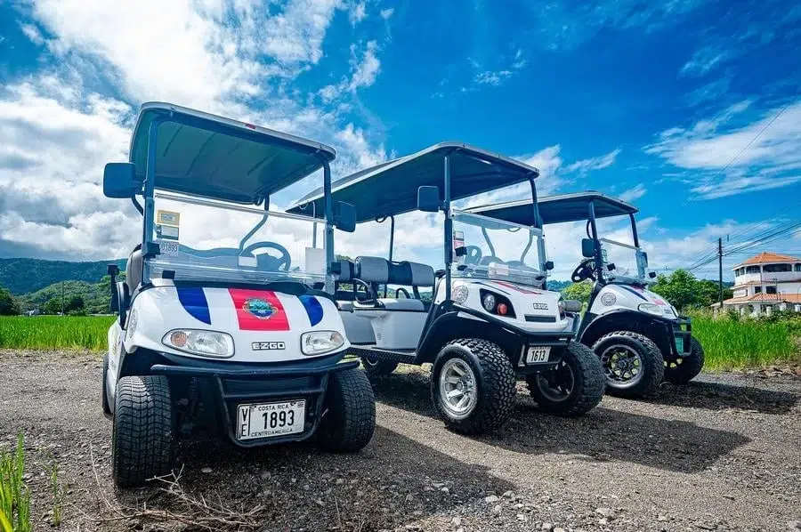 sports and adventure photography costa rica -2 | Pacific Photography Three white golf carts parked on a gravel lot under a bright blue sky, facing left in a row.