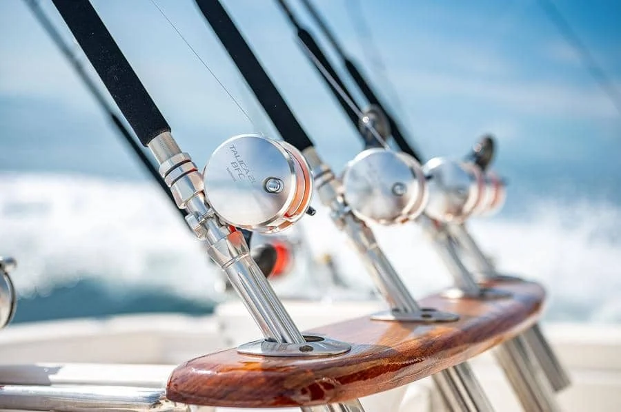 sports and adventure photography costa rica -4 | Pacific Photography Close-up of polished fishing rod holders and reel handles mounted on a wooden boat railing, with water in the blurred background.