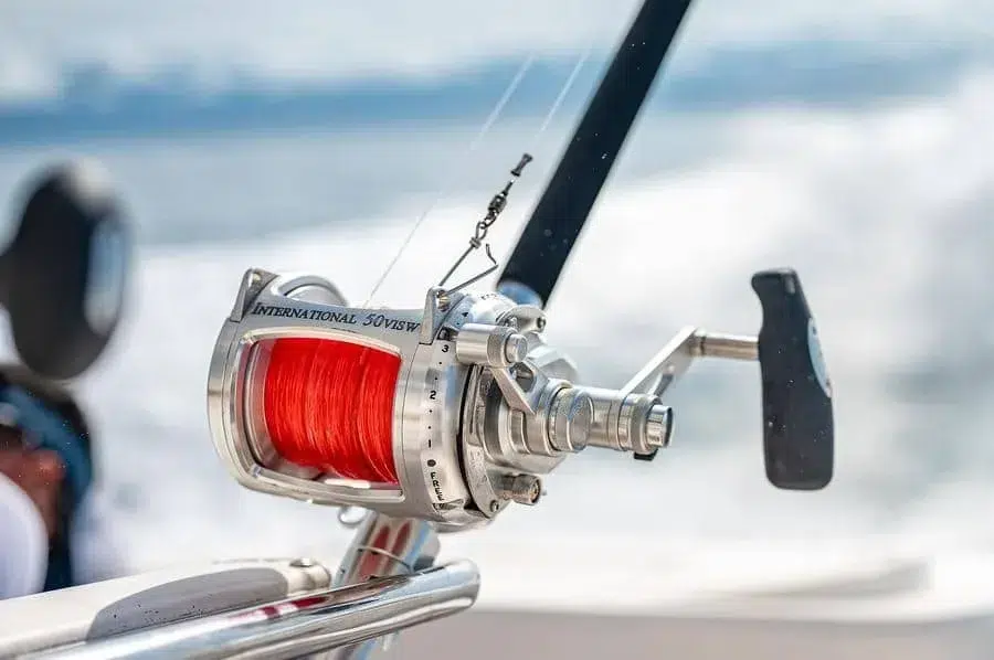 sports and adventure photography costa rica -5 | Pacific Photography Close-up of a silver fishing reel with bright red line mounted on a boat rod, water blurred in the background.