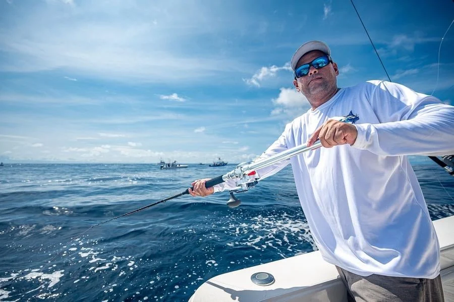sports and adventure photography costa rica -6 | Pacific Photography Man fishing from a boat on the open blue ocean, reeling in a fishing line under a sunny sky.