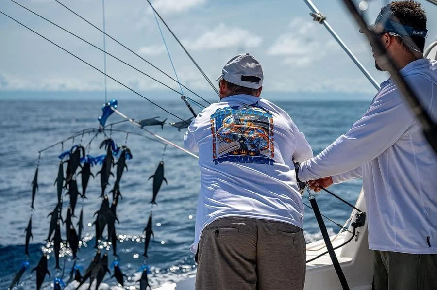 sports and adventure photography costa rica -7 | Pacific Photography Two fishermen on a boat at sea reel in lines, with a row of hanging fish seen along the rigging behind them.