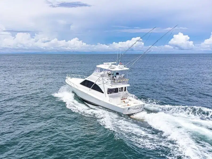 sports and adventure photography costa rica -8 | Pacific Photography White motor yacht cruising through blue ocean with wake and fishing rods mounted on top, cloudy sky ahead