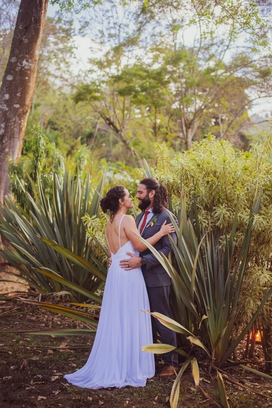 wedding ceremony photography costa rica-2 | Pacific Photography Couple in wedding attire embracing in a garden among tall green plants and trees, smiling at each other.