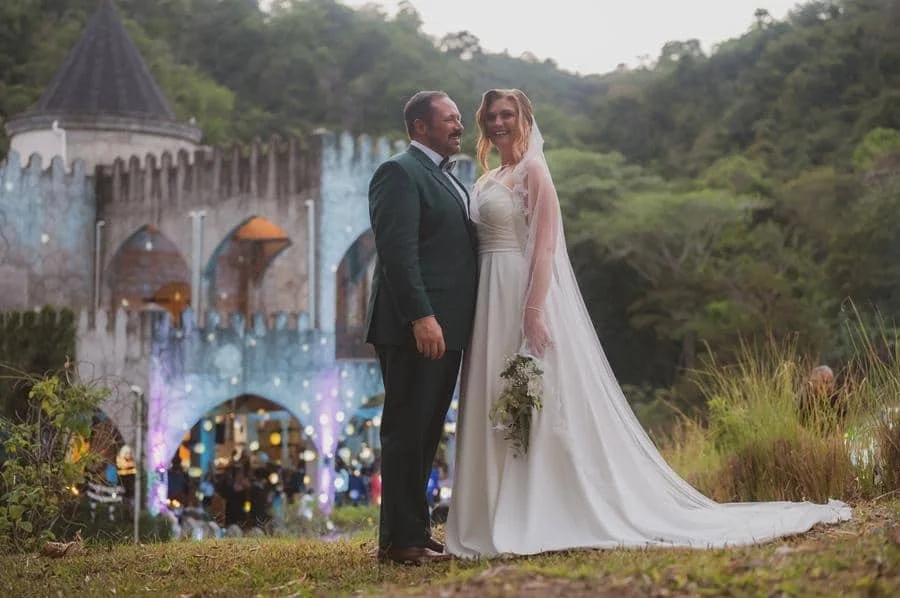 wedding ceremony photography costa rica-22 | Pacific Photography Bride and groom pose outdoors in wedding attire with a castle venue in the background, smiling at each other.