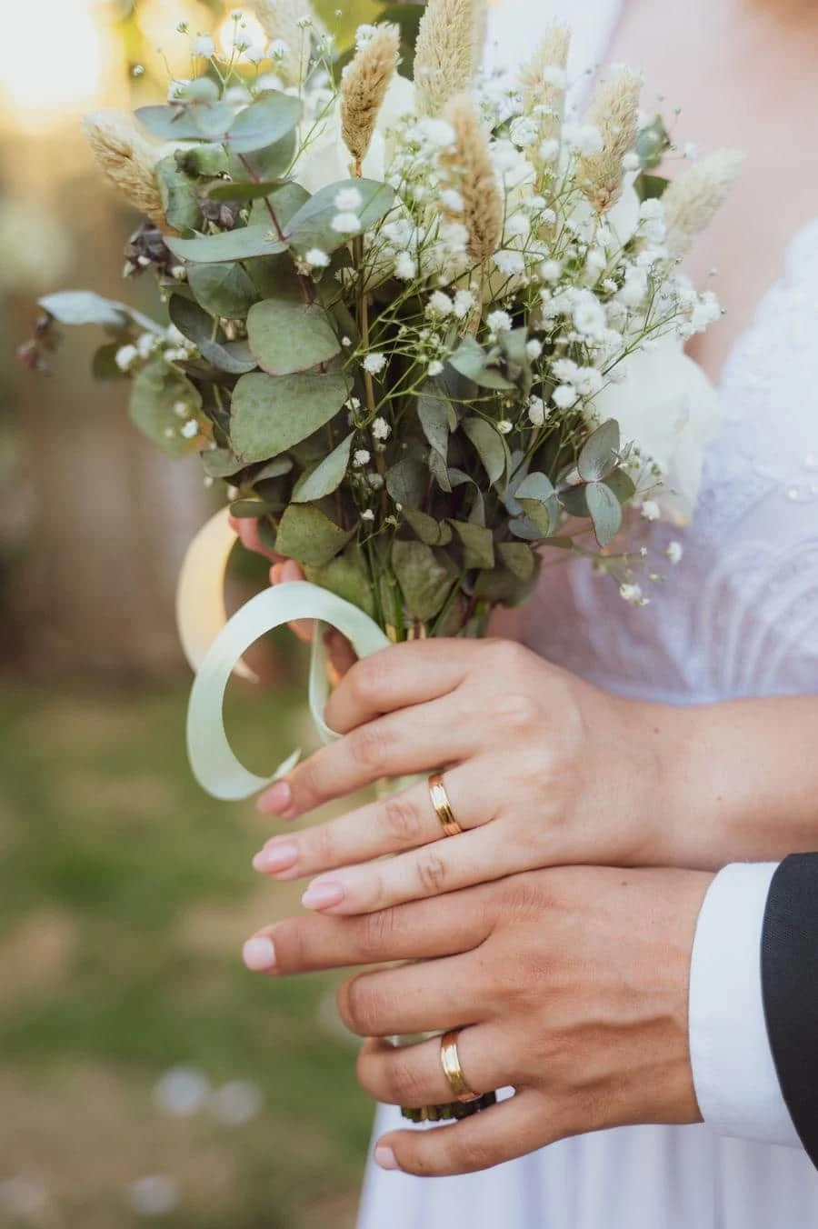 wedding ceremony photography costa rica-24 | Pacific Photography Close-up of a bride and groom holding a bouquet of eucalyptus, baby's breath, and dried grasses, with wedding rings visible.