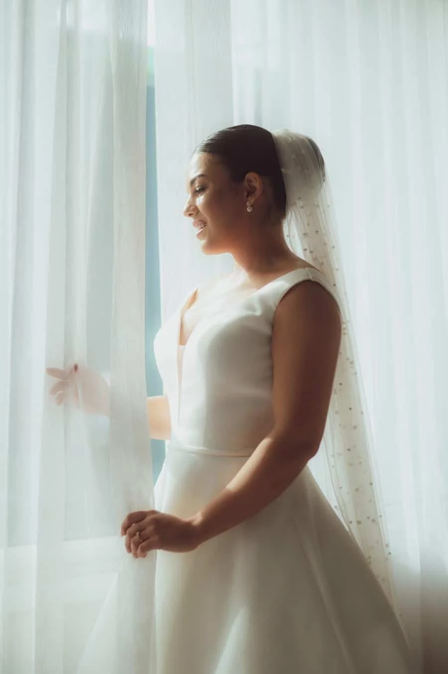 wedding prep photography costa rica-15 | Pacific Photography Bride in a white wedding gown and veil stands by a window, looking out.