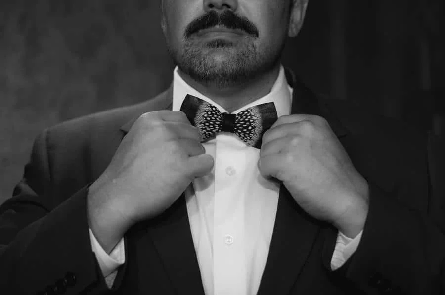 wedding prep photography costa rica-21 | Pacific Photography Man in a suit adjusts a patterned bow tie, mustache visible in a black-and-white photo.