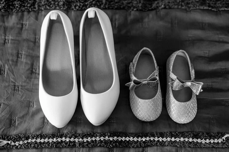 wedding prep photography costa rica-25 | Pacific Photography White women's flats and two small glittery baby shoes with bows lined up on a dark fabric background.