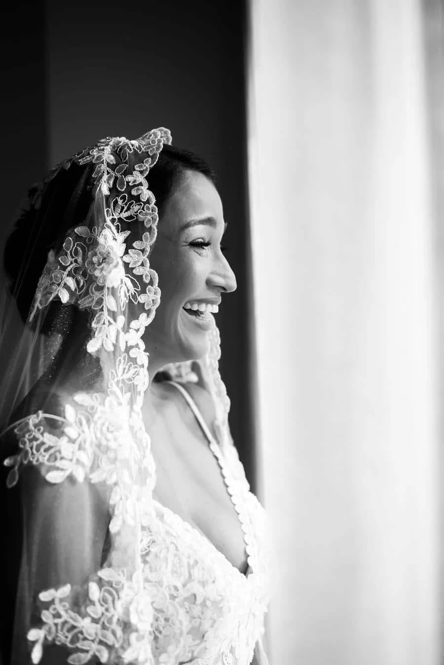 wedding prep photography costa rica-3 | Pacific Photography Black-and-white profile of a smiling bride wearing a floral lace veil and wedding dress by a window lightStyling detail-focused portrait