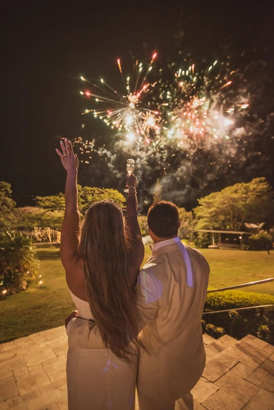 wedding reception and party photography in costa rica -2 | Pacific Photography Couple in formal attire from behind raising a toast as fireworks explode in the night sky.