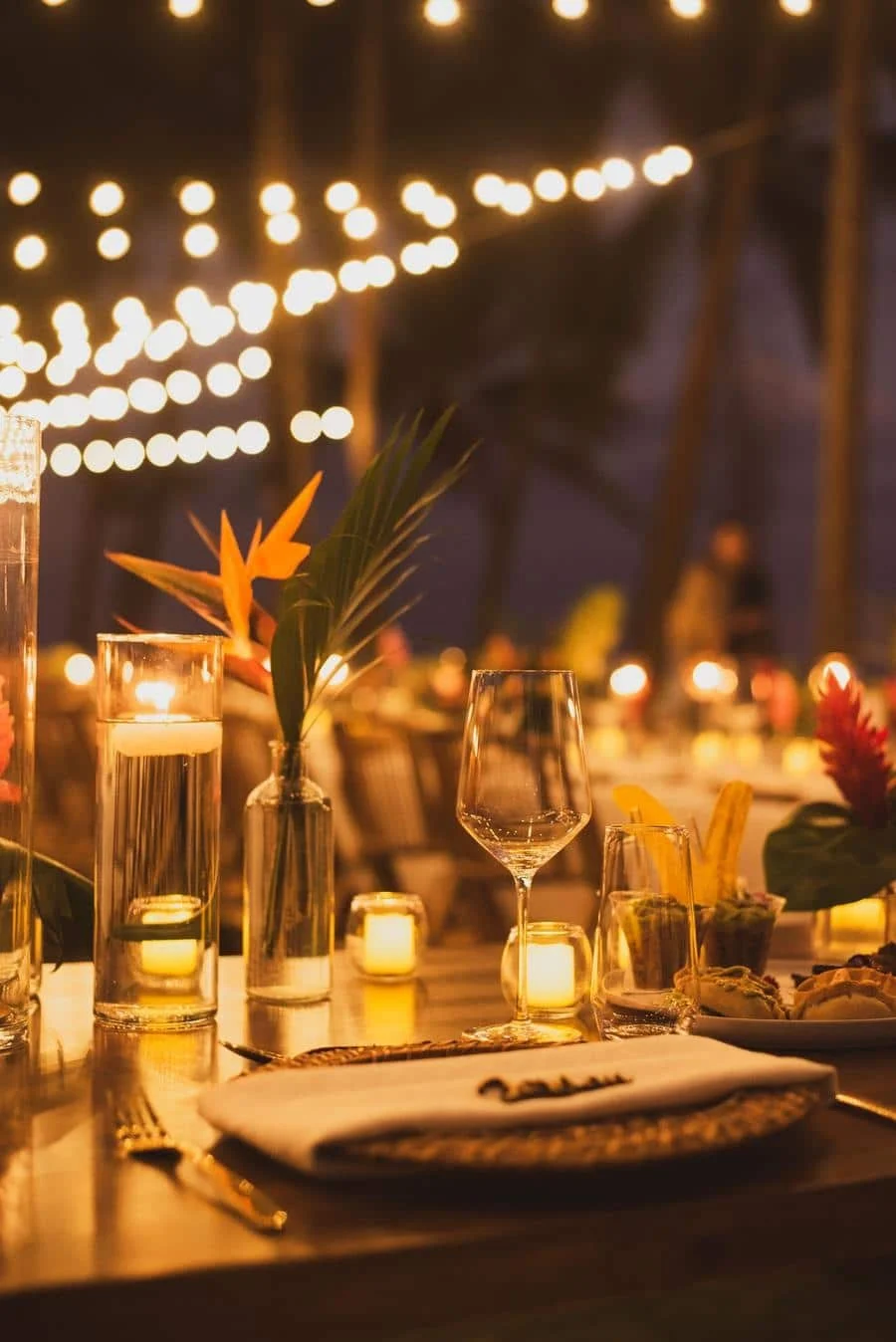 wedding reception and party photography in costa rica -3 | Pacific Photography Romantic candlelit dinner setup with wine glasses and soft bokeh string lights in the background.